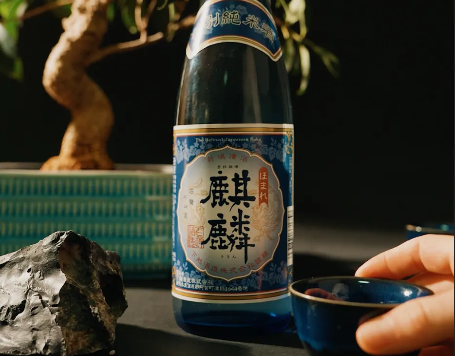 Bouteille de saké et coupelle sur une table, un bonsaï en arrière-plan