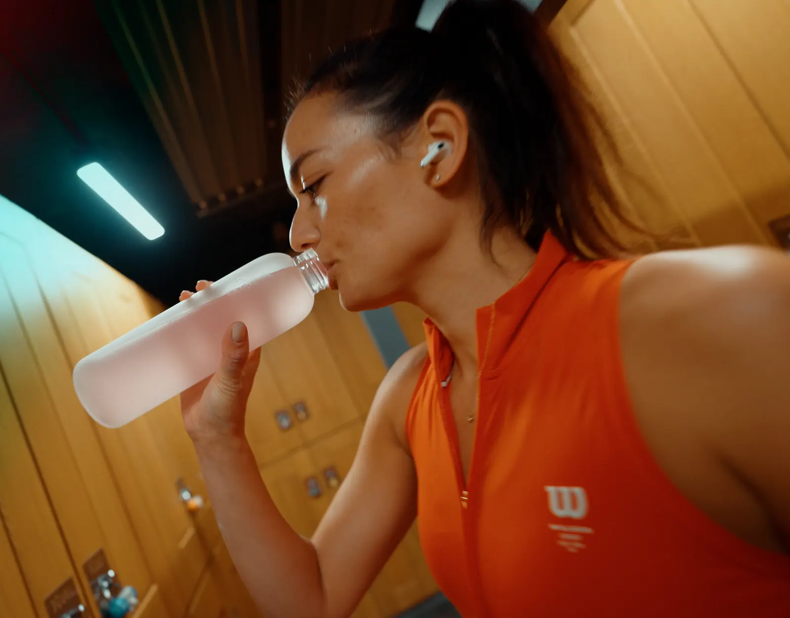 Sportive en débardeur orange buvant à sa gourde dans un vestiaire