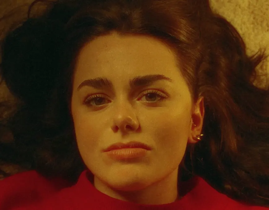 Portrait d’une femme allongée, cheveux étalés, pull rouge, lumière chaude