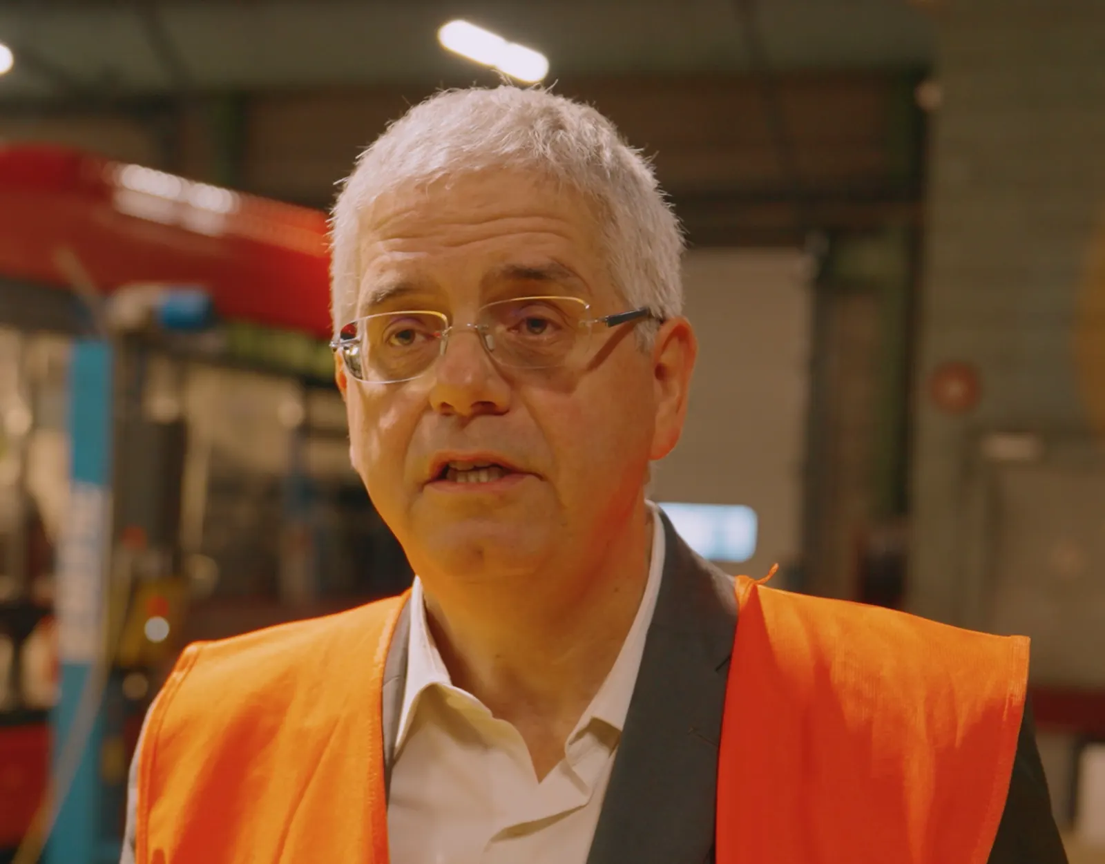 Homme en gilet orange interviewé dans un atelier