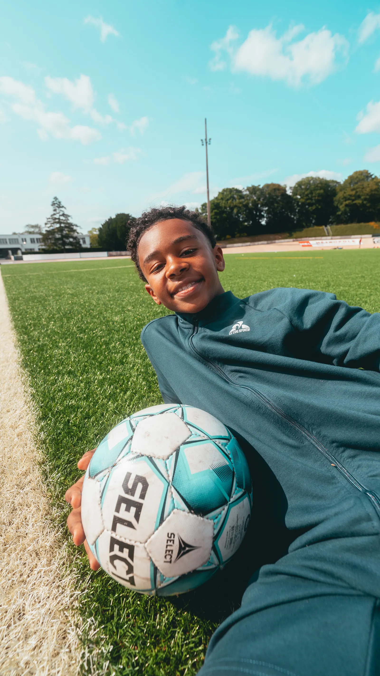 Un enfant allongé dans l’herbe sourit, un ballon de football à la main